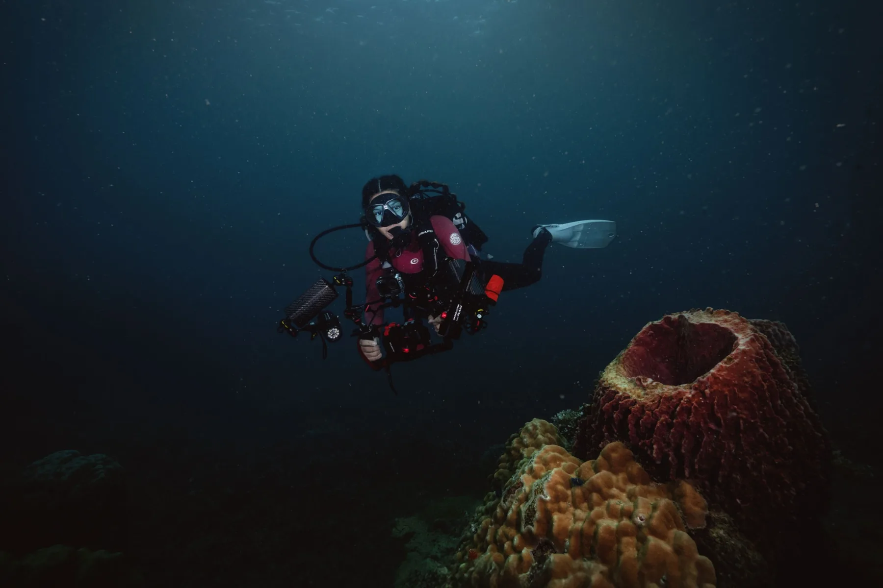 female scuba diver holding underwater camera rig on a coral reef 