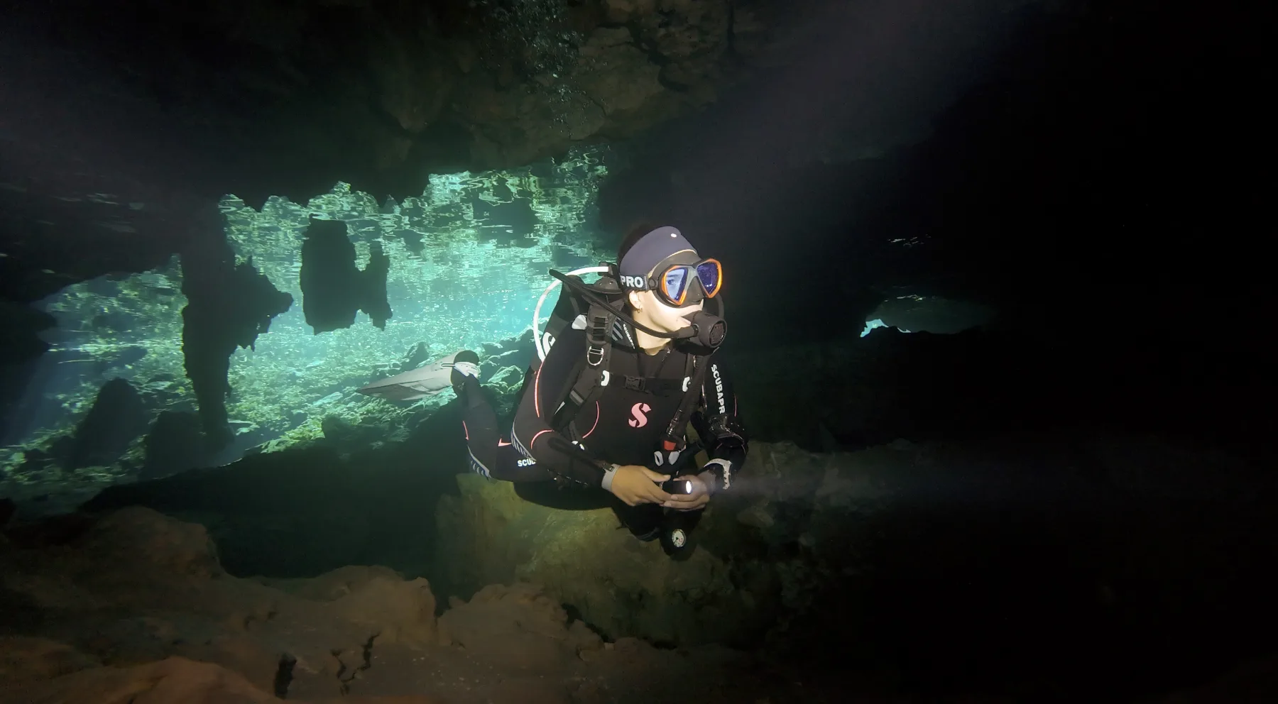 A scuba diver with a torch swimming through a cenote cavern in Mexico