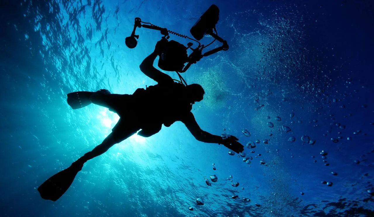 An underwater photographer diving with a camera rig and strobes