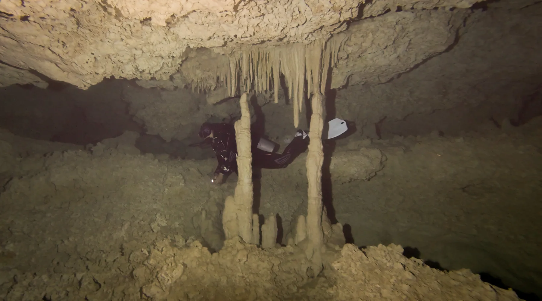 A scuba diver swimming past limestone columns in a Mexican cenote