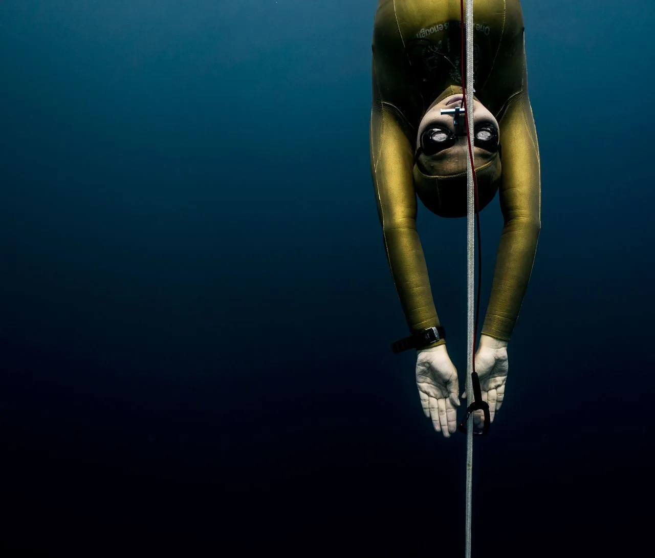 Freediver in gold wetsuit descends with rope in Bali's blue waters, showcasing underwater exploration