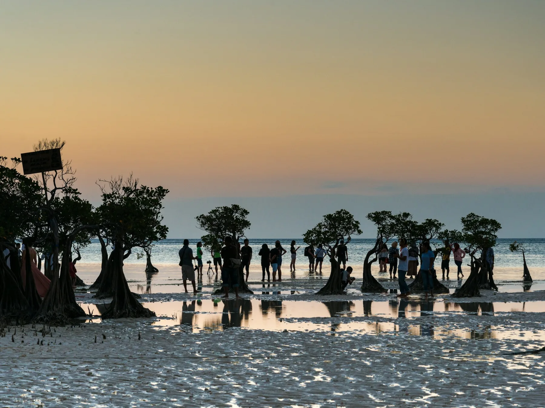 un grupo de personas de pie sobre una playa de arena al atardecer en la playa de Walakiri, en Nusa Tenggara Oriental