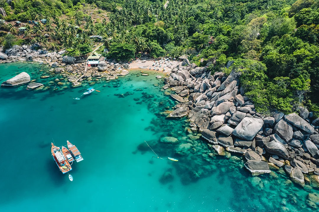 Aerial view of a granite-boulder bay on the east coast of Koh Tao, the kind of sheltered cove that gives the island its mix of reef and headland diving.