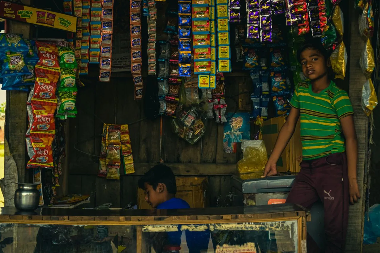 two indian boys in a rural store surrounded by sachet packaged products