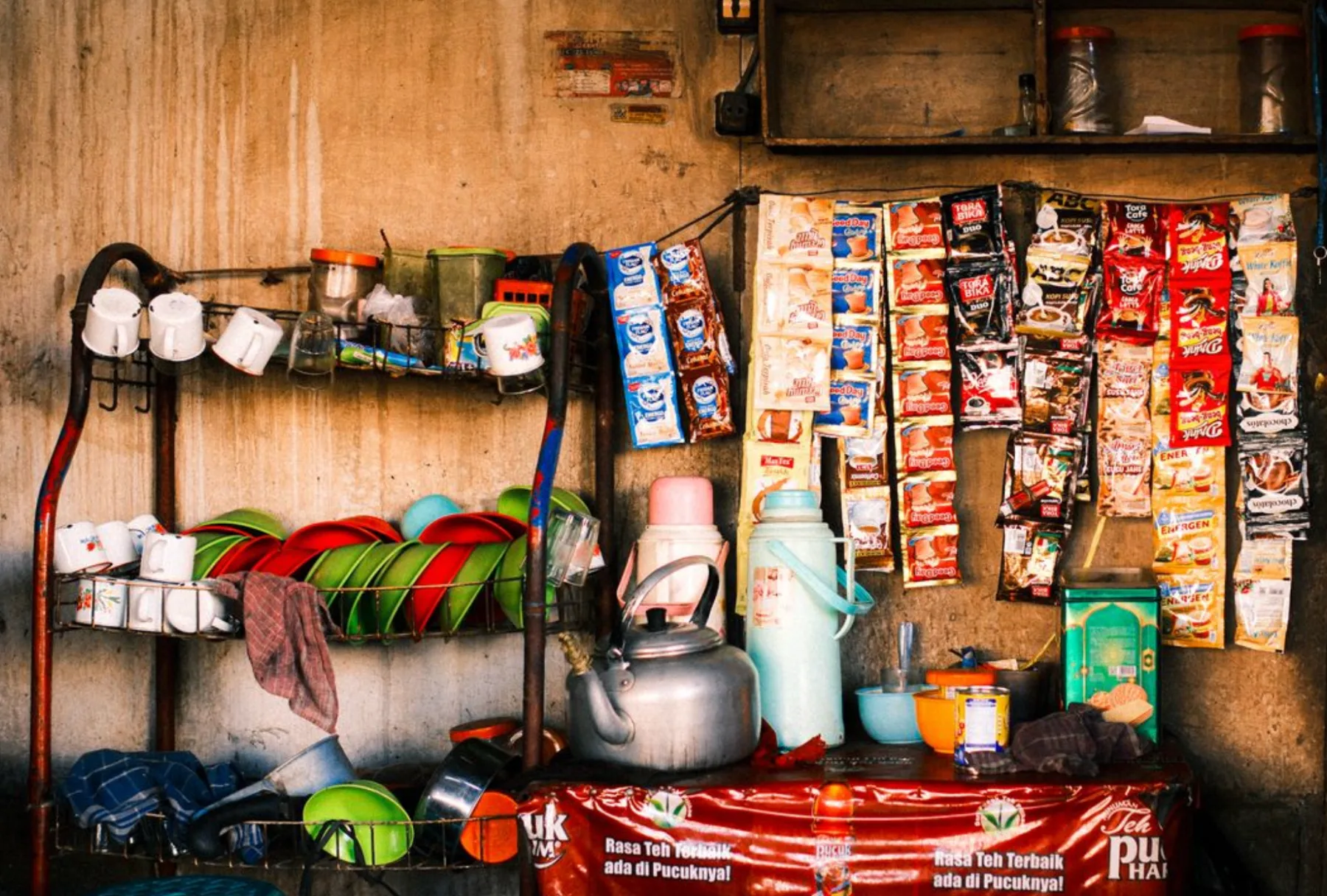 A colorful display of a traditional Indonesian street vendor's stall with assorted goods in sachet packaging and kitchenware.
