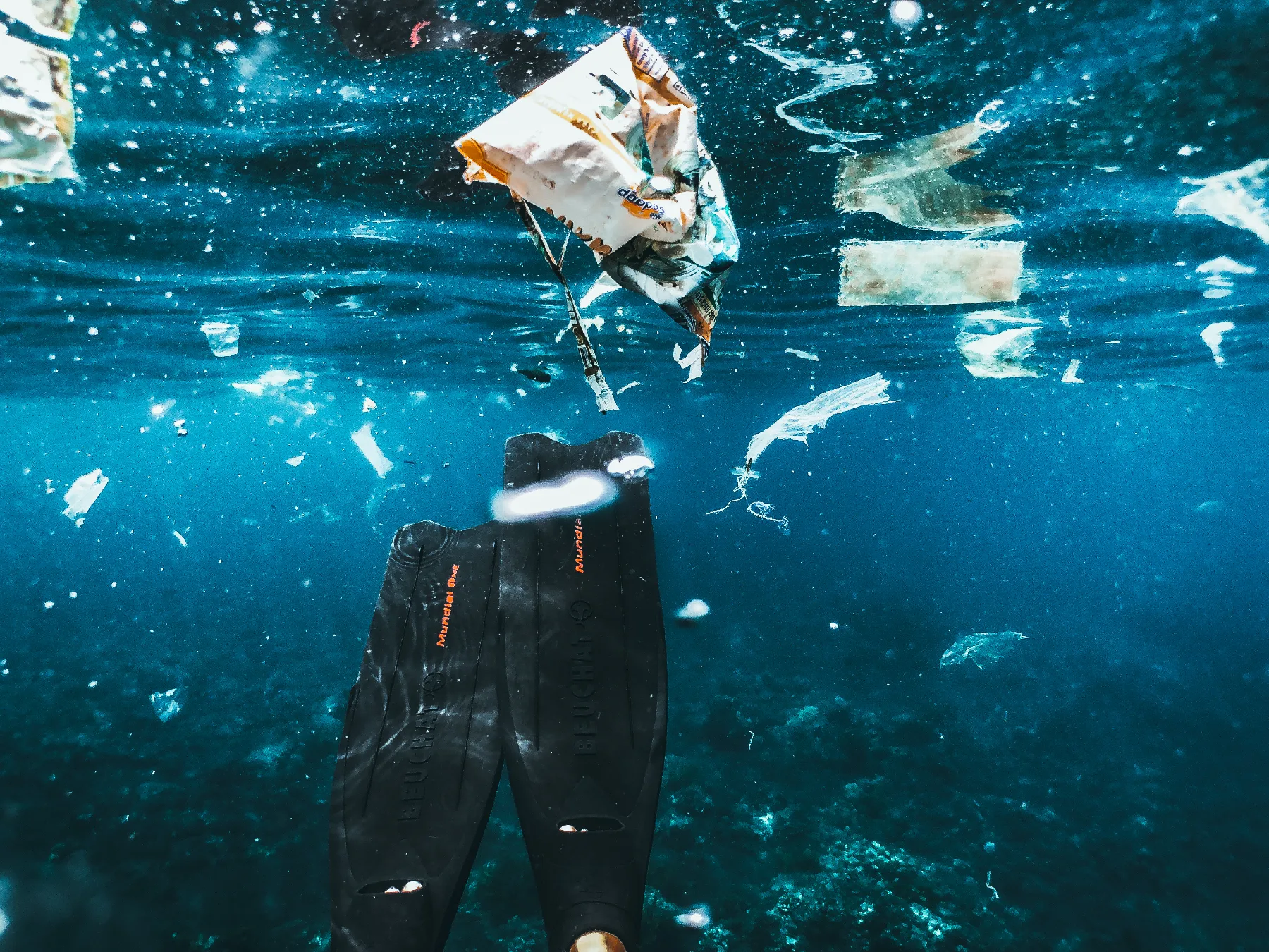 underwater shot of diving fins and plastic pollution in the ocean from the perspective of a diver