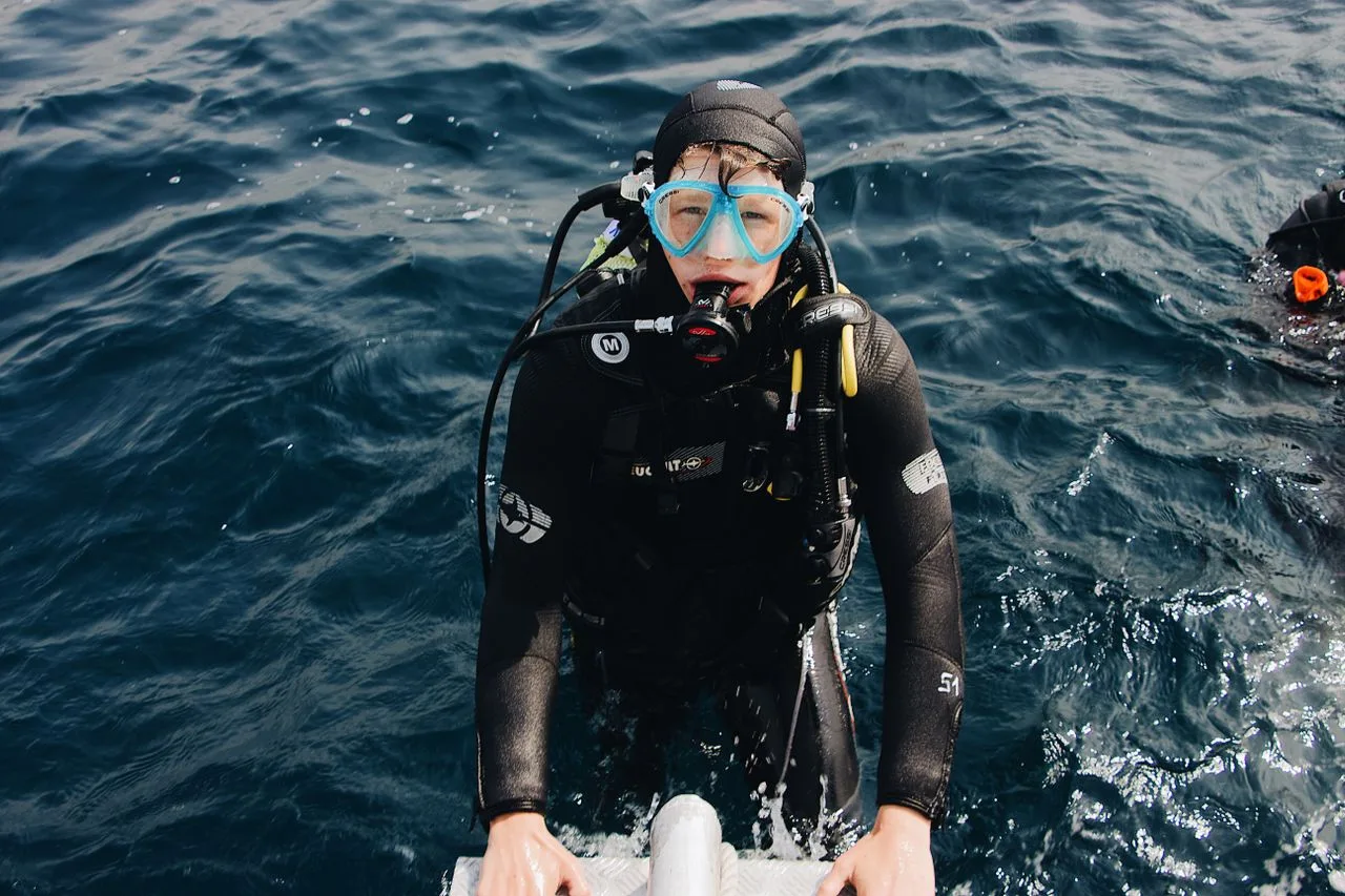 male scuba diver in the ocean climbing up the ladder of a dive boat