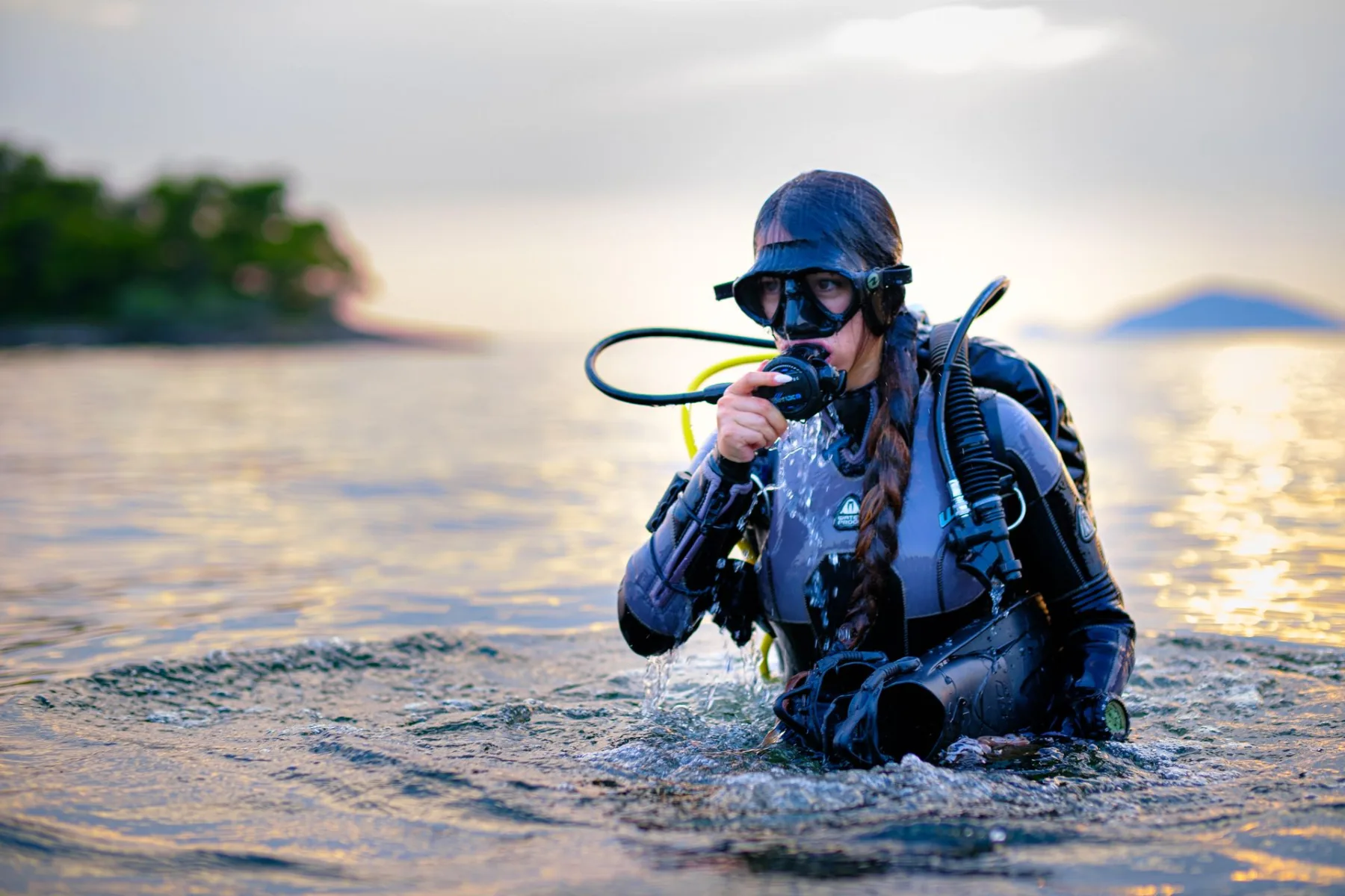 Female scuba diver wearing diving gear in the ocean during sunset
