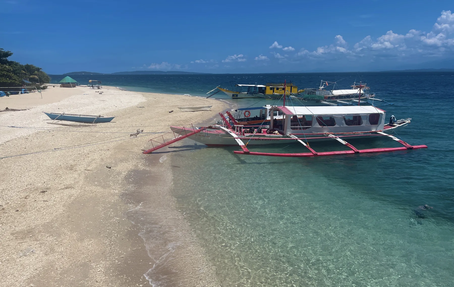 Bancas tradicionales de buceo varadas en una playa de arena blanca en Verde Island, Filipinas, la flota de excursiones de un día que opera los sitios mar adentro.