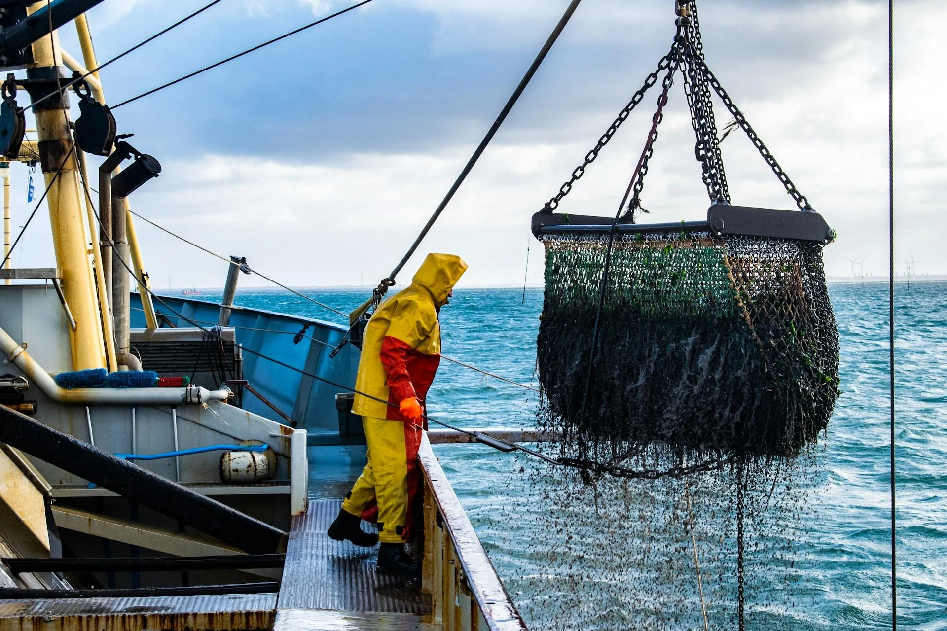 Un pescador con impermeables amarillos en la cubierta de un arrastrero mientras una red de arrastre es izada por una grúa, chorreando agua de mar: uno de los métodos de pesca más destructivos que aún opera dentro de áreas marinas protegidas.