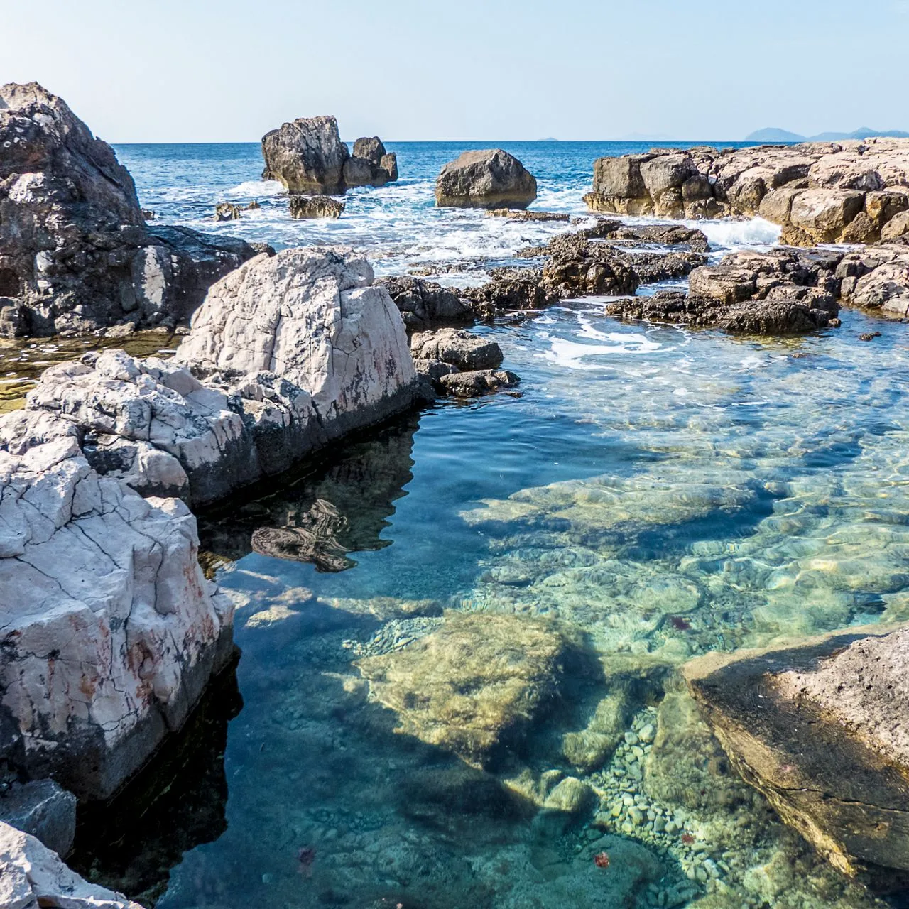 A beautiful rocky seascape showcasing clear waters and a scenic shoreline under a bright sky
