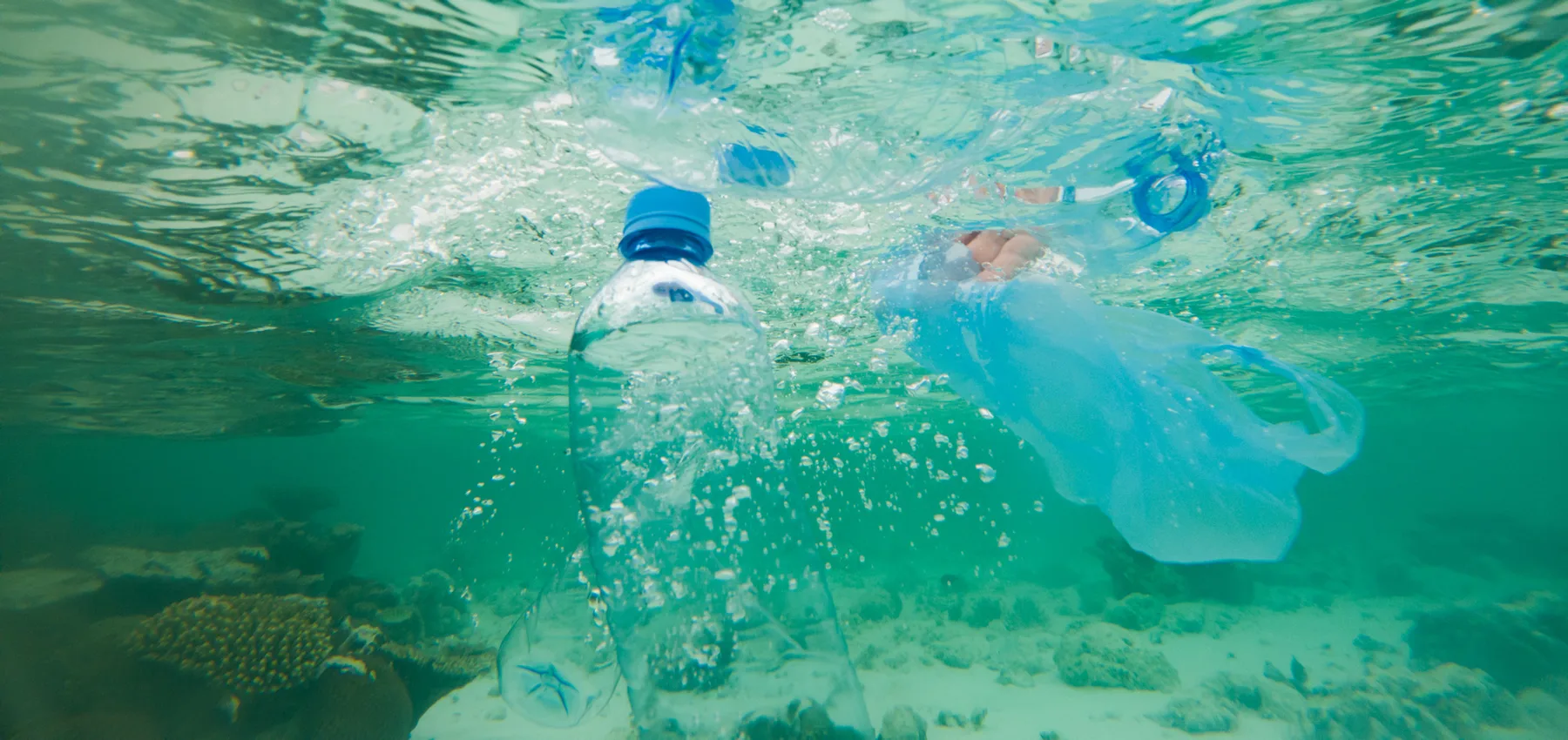 Una botella plástica de agua y una bolsa plástica traslúcida flotando justo bajo la superficie del agua sobre un arrecife de coral, los desechos cotidianos que ahora son parte de casi toda visita a un arrecife.