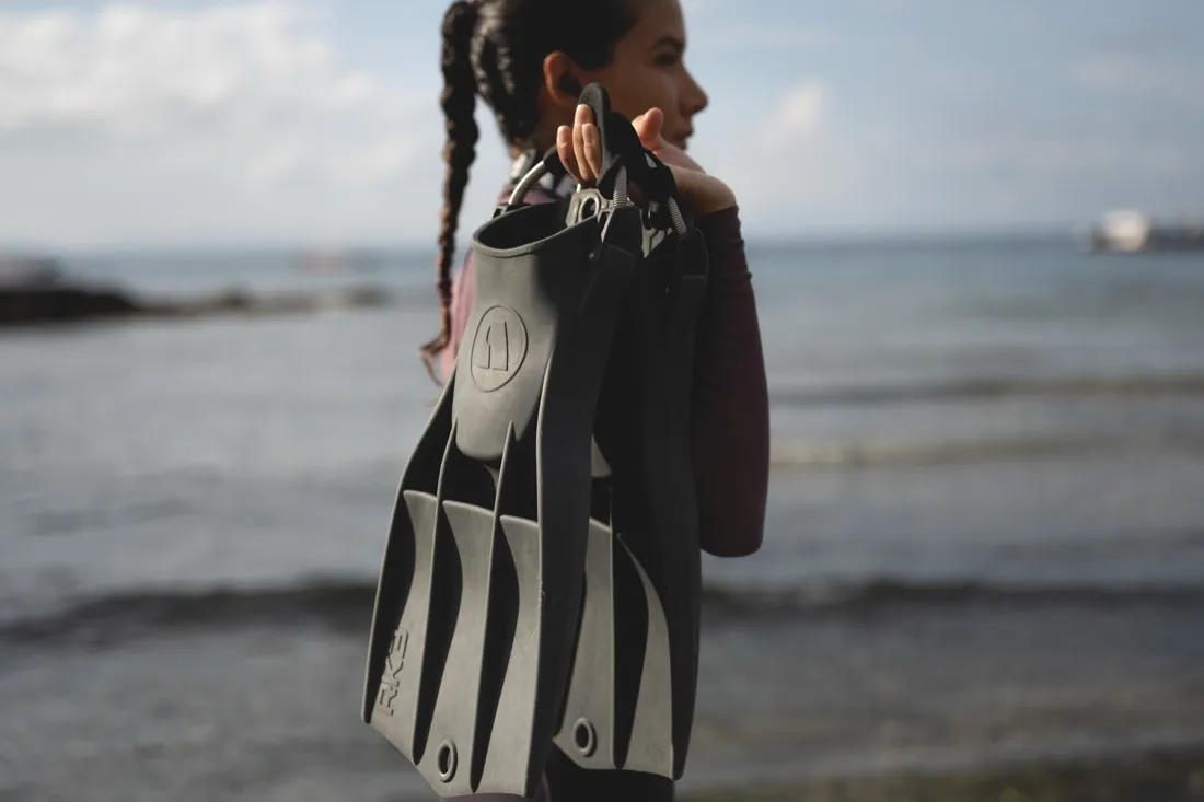 Caro Santamaria holding grey Apeks RK3 fins on the beach