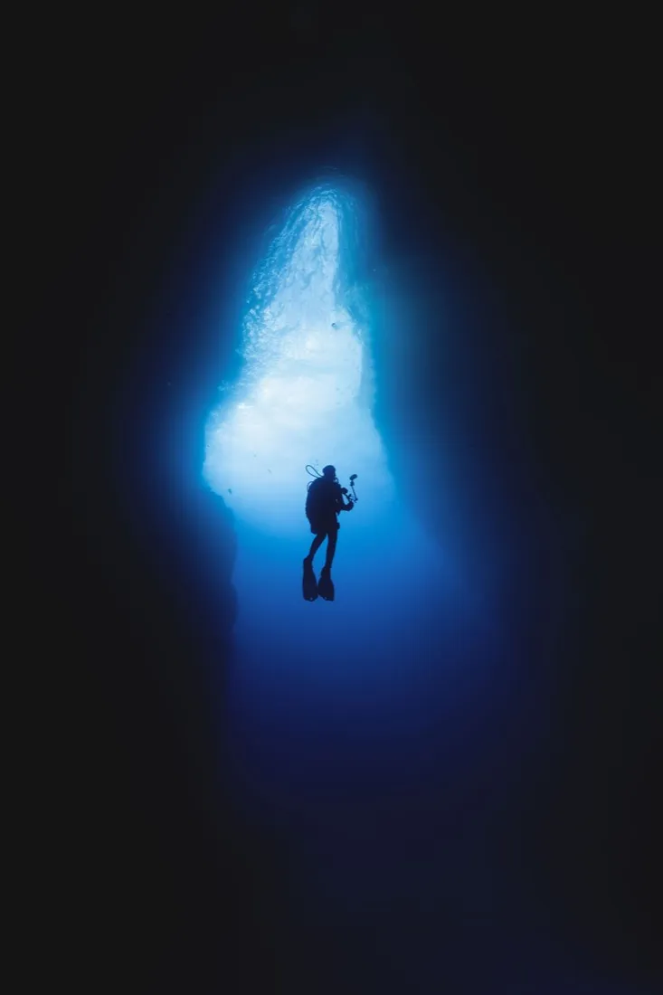 A scuba diver silhouetted in a cavern of blue light